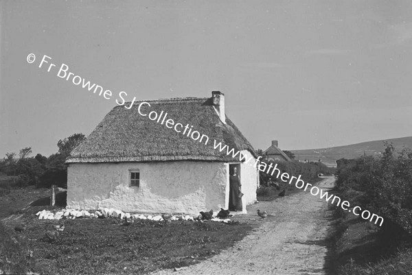 WOMAN AT DOOR OF WHITEWASHED COTTAGE